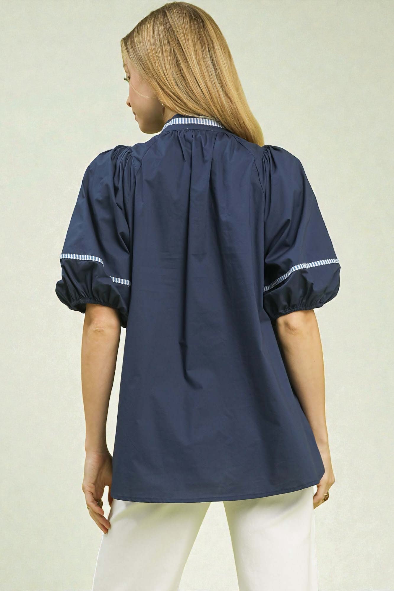 Woman wearing a navy blue blouse with white trim on a beige background