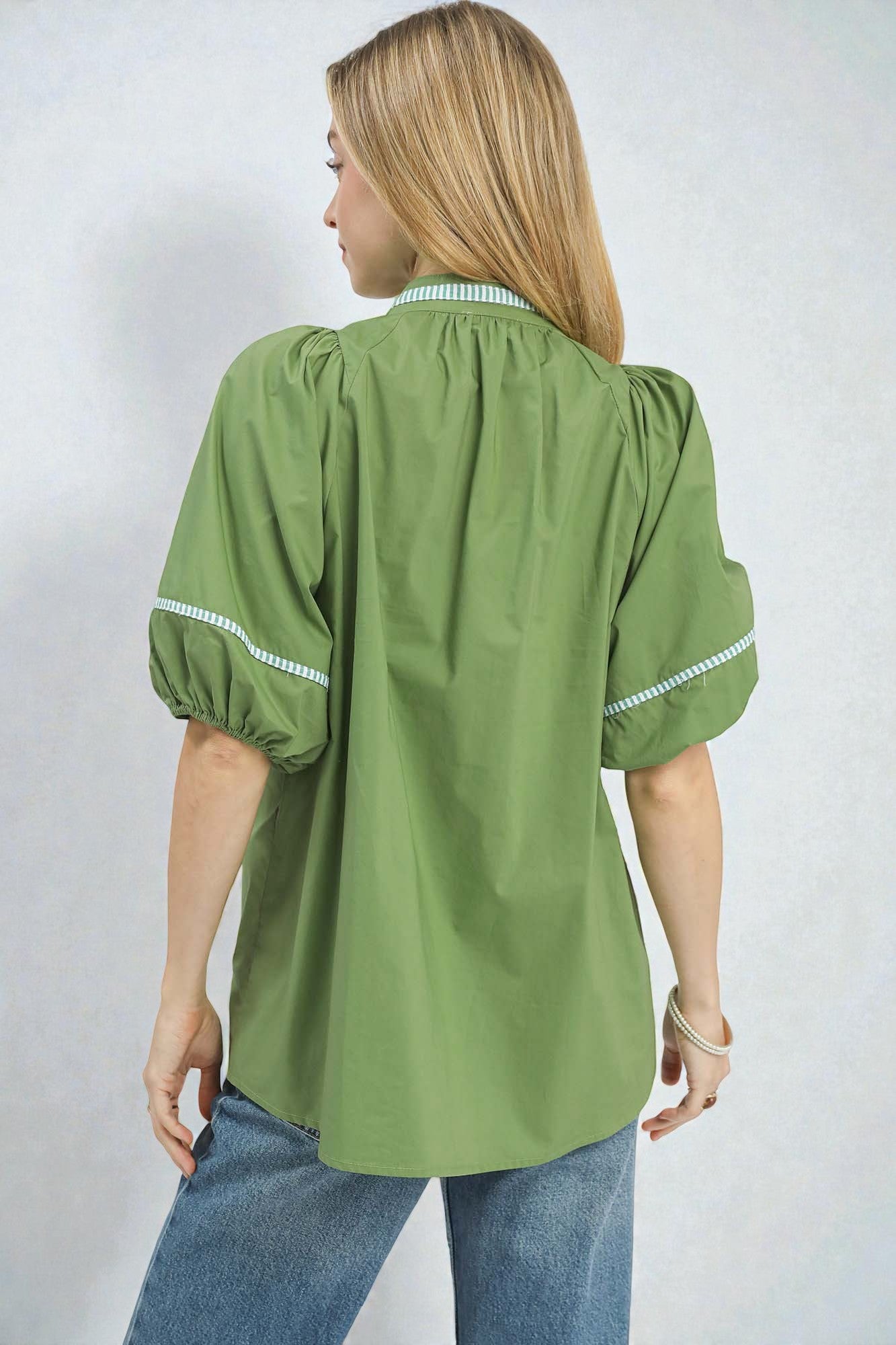 Woman wearing a green blouse with white trim on a plain background
