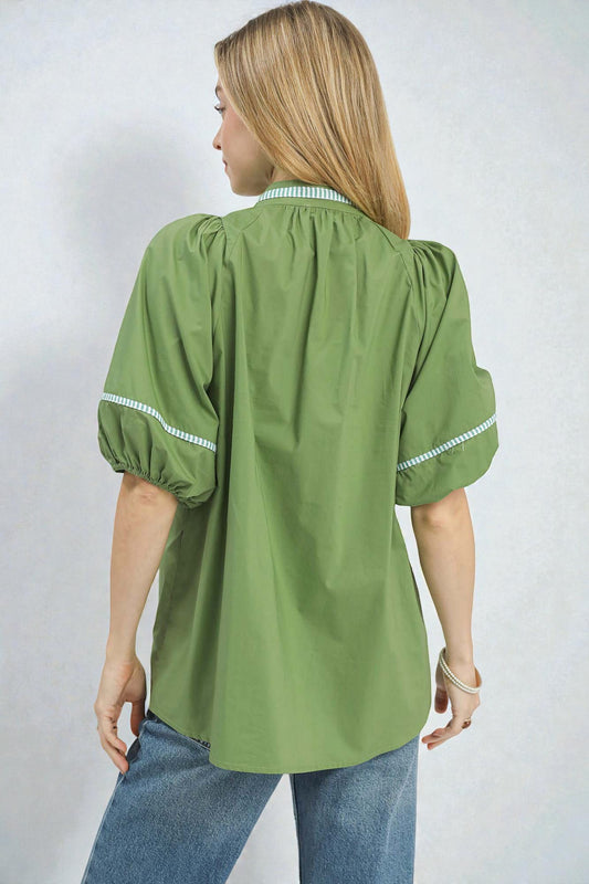 Woman wearing a green blouse with white trim on a plain background