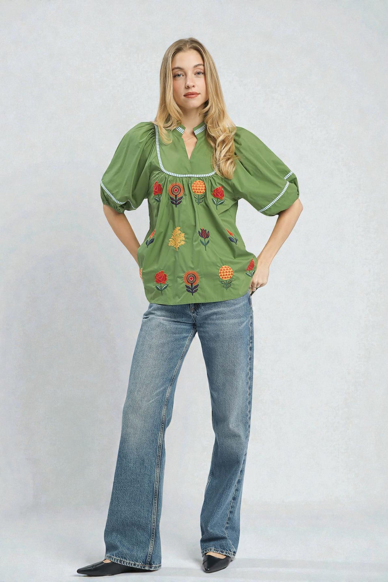 Woman wearing a green embroidered blouse and blue jeans on a white background