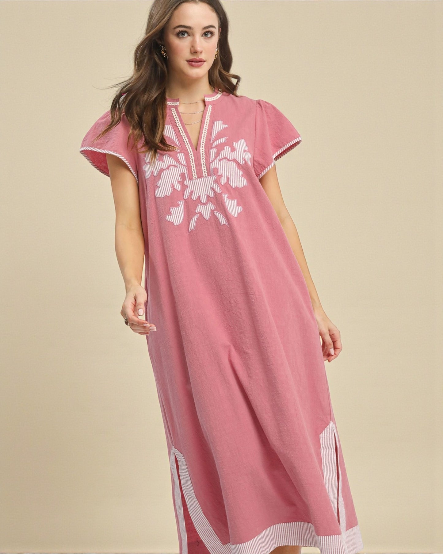 Woman wearing a pink dress with white embroidery on a beige background