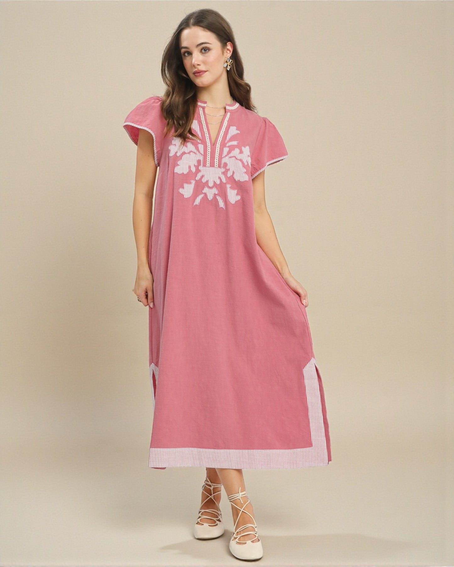 Woman wearing a pink dress with white floral embroidery on a beige background