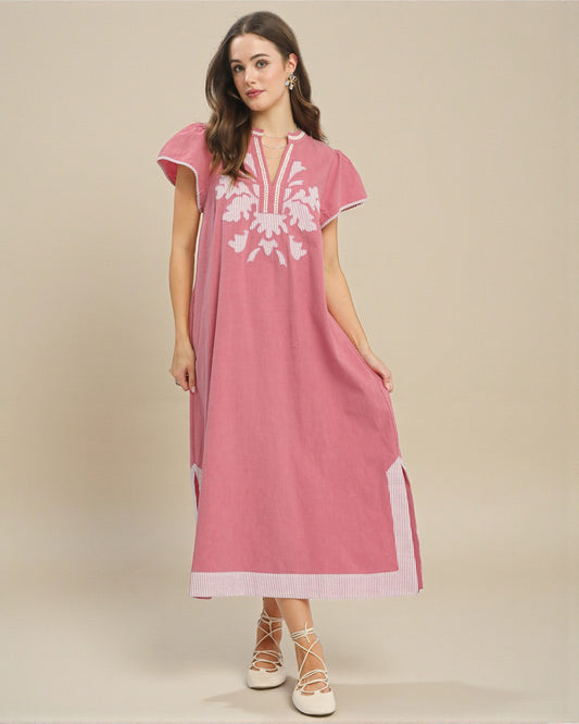 Woman wearing a pink dress with white floral embroidery on a beige background