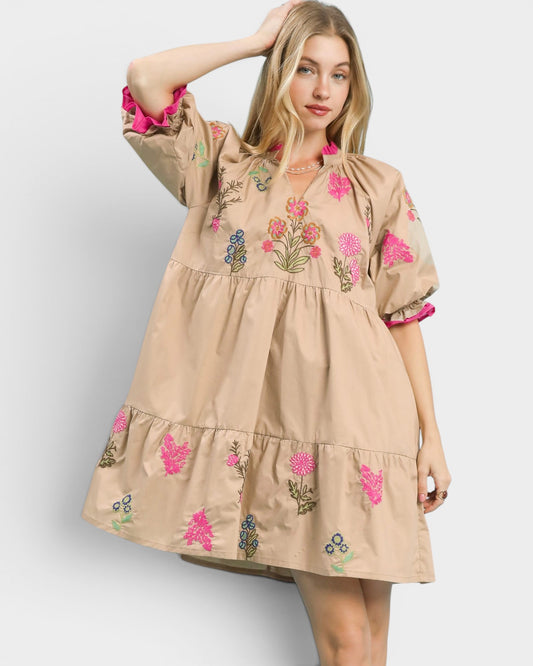 Woman wearing a beige dress with floral embroidery on a white background