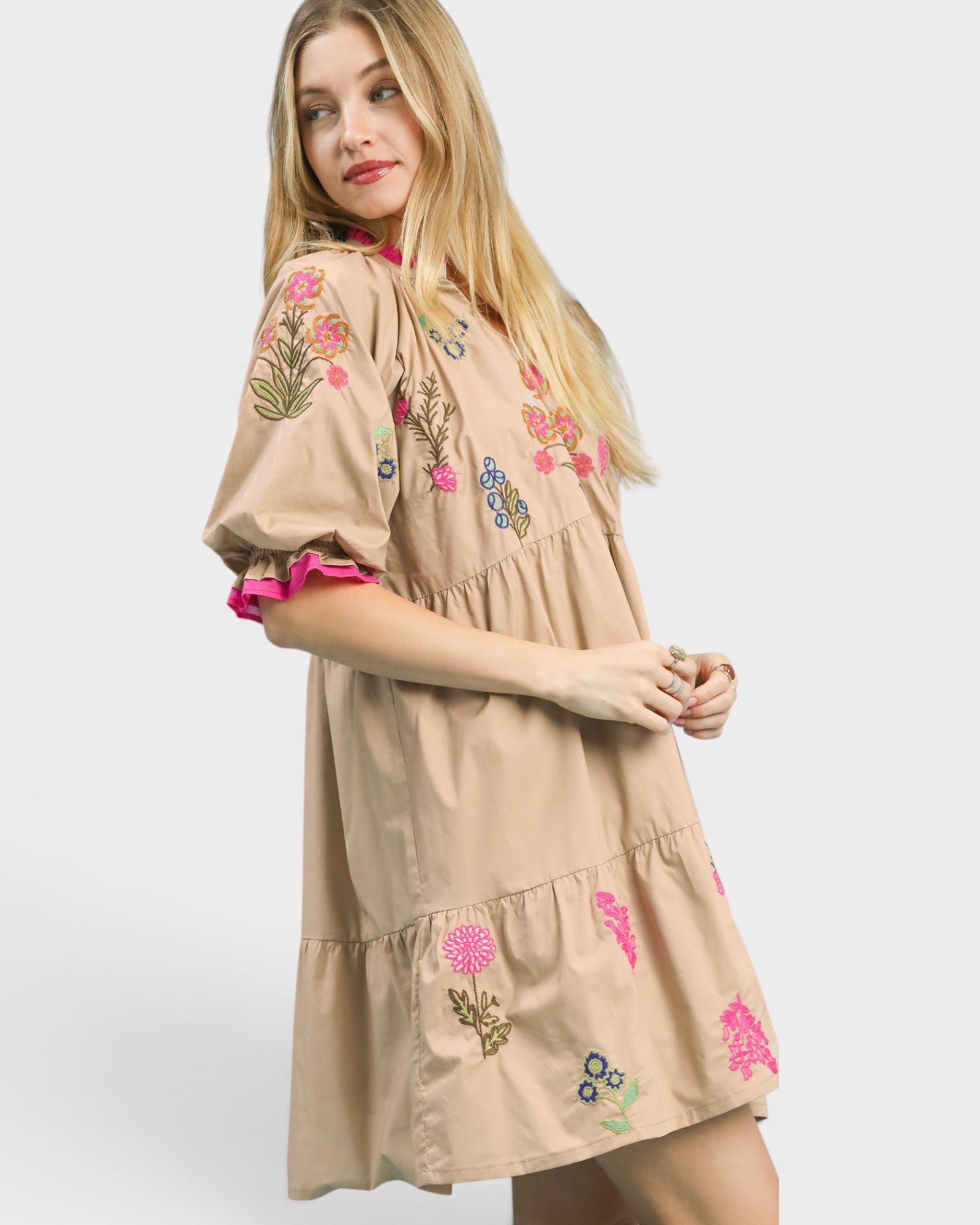 Woman wearing a beige dress with floral embroidery on a white background