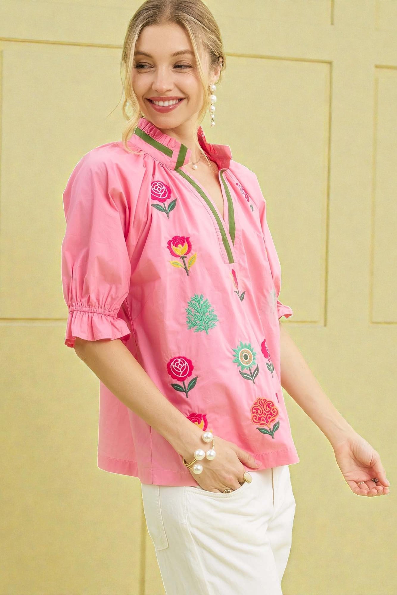 Woman wearing a pink embroidered blouse against a yellow wall