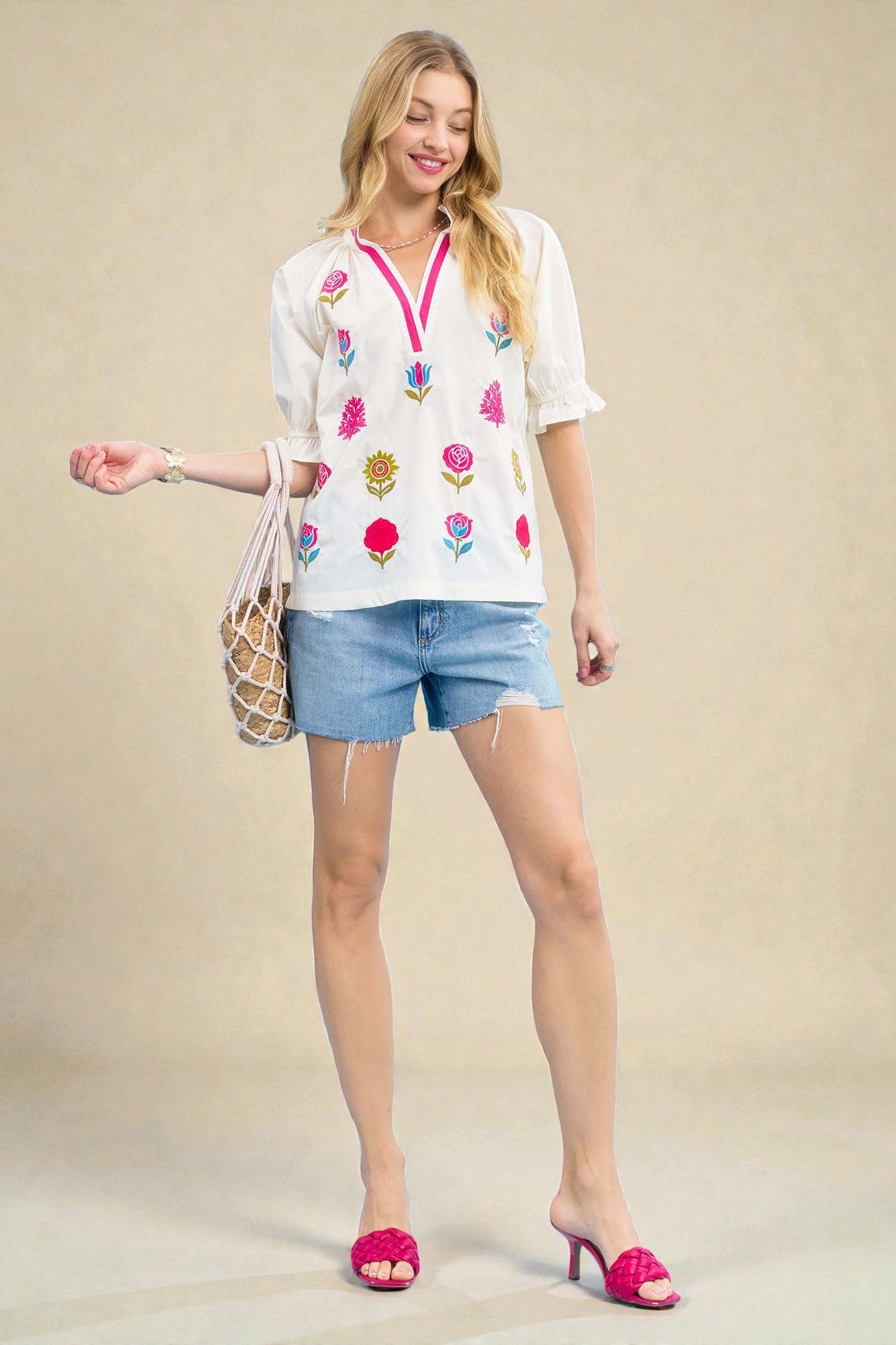 Woman wearing a floral embroidered top and denim shorts with a beige background