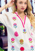 Woman wearing a white blouse with colorful floral patterns in an outdoor setting