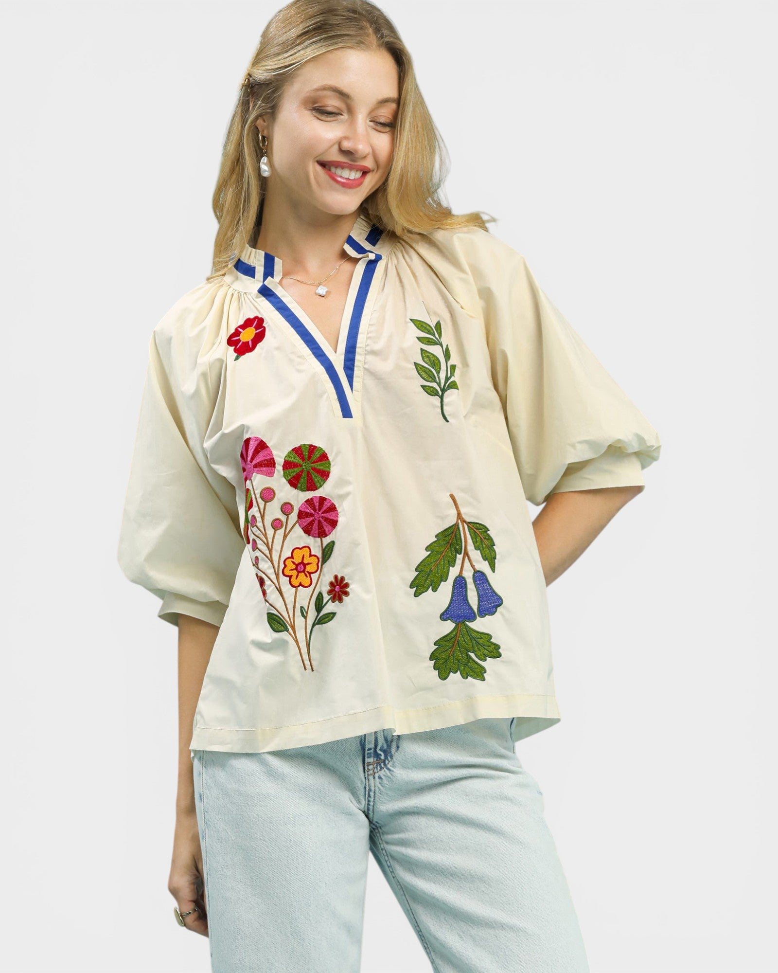 Woman wearing a cream blouse with floral embroidery on a plain background