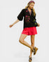 Woman wearing a black embroidered top and red shorts on a white background