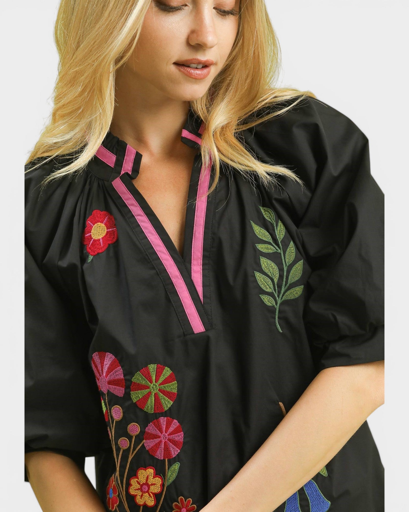 Black blouse with colorful floral embroidery worn by a model on a white background