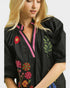 Black blouse with colorful floral embroidery worn by a model on a white background