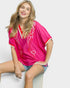 Woman wearing a bright pink top with white patterns sitting on a white chair.