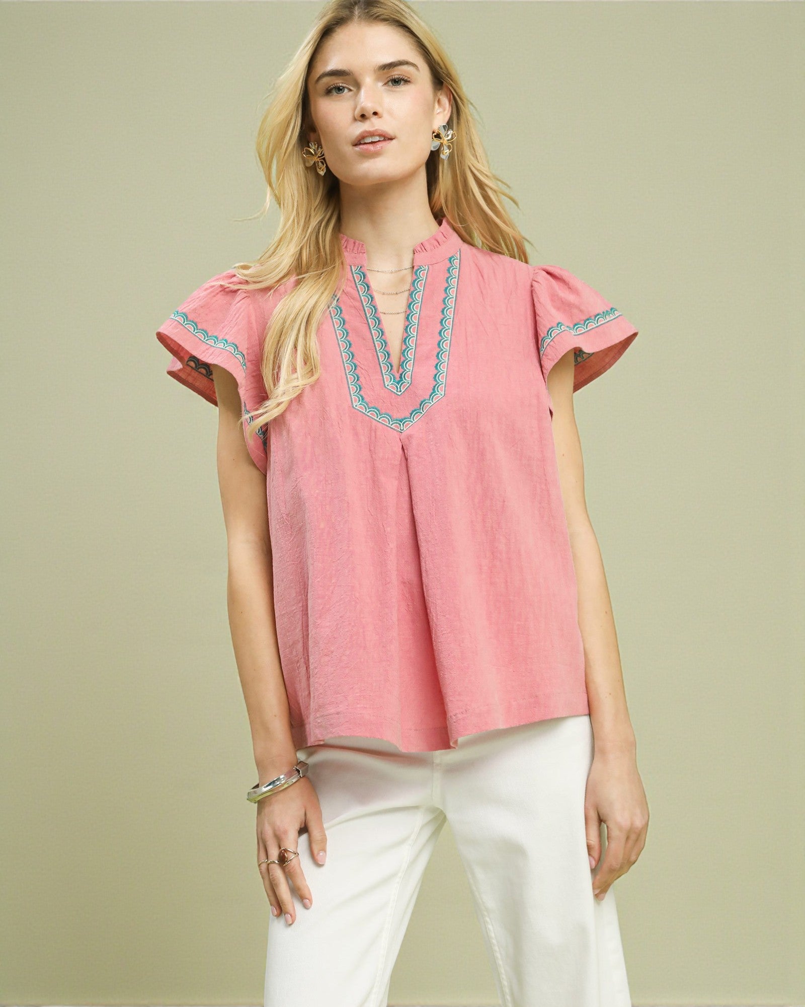 Woman wearing a pink blouse with blue embroidery on a beige background