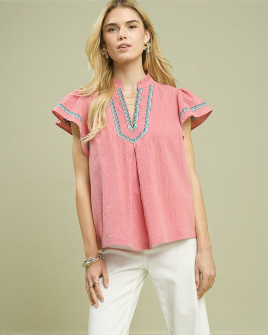 Woman wearing a pink blouse with blue embroidery on a beige background