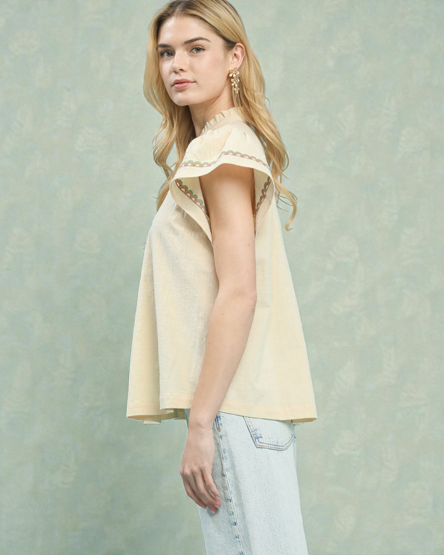 Woman wearing a light yellow sleeveless top with lace details against a textured light green background