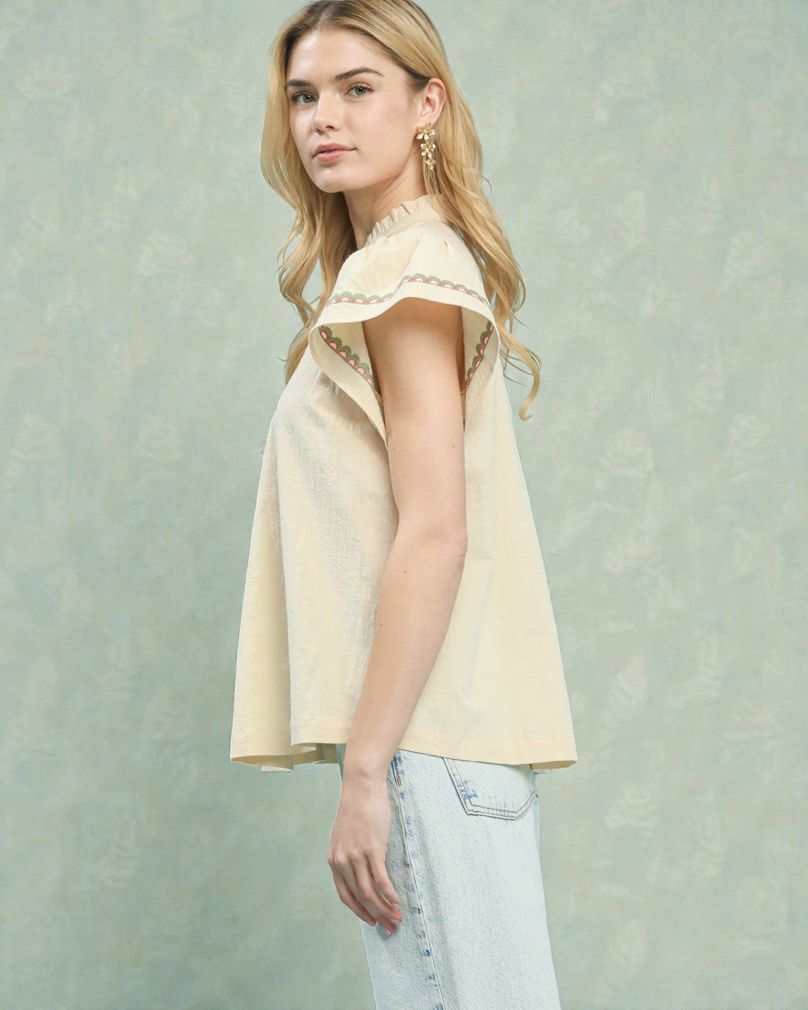 Woman wearing a light yellow sleeveless top with lace details against a textured light green background