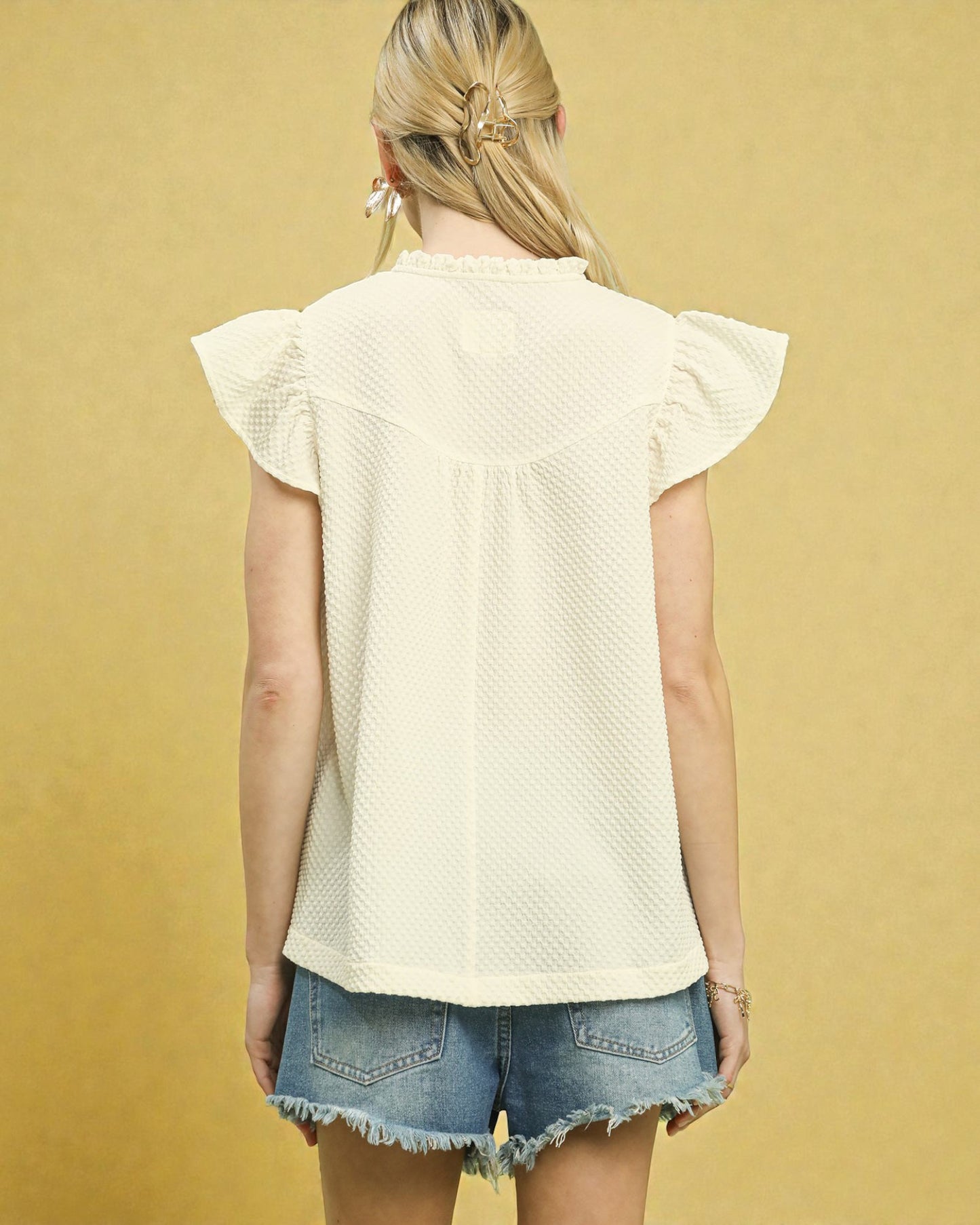 Woman wearing a light-colored top and denim shorts against a yellow background