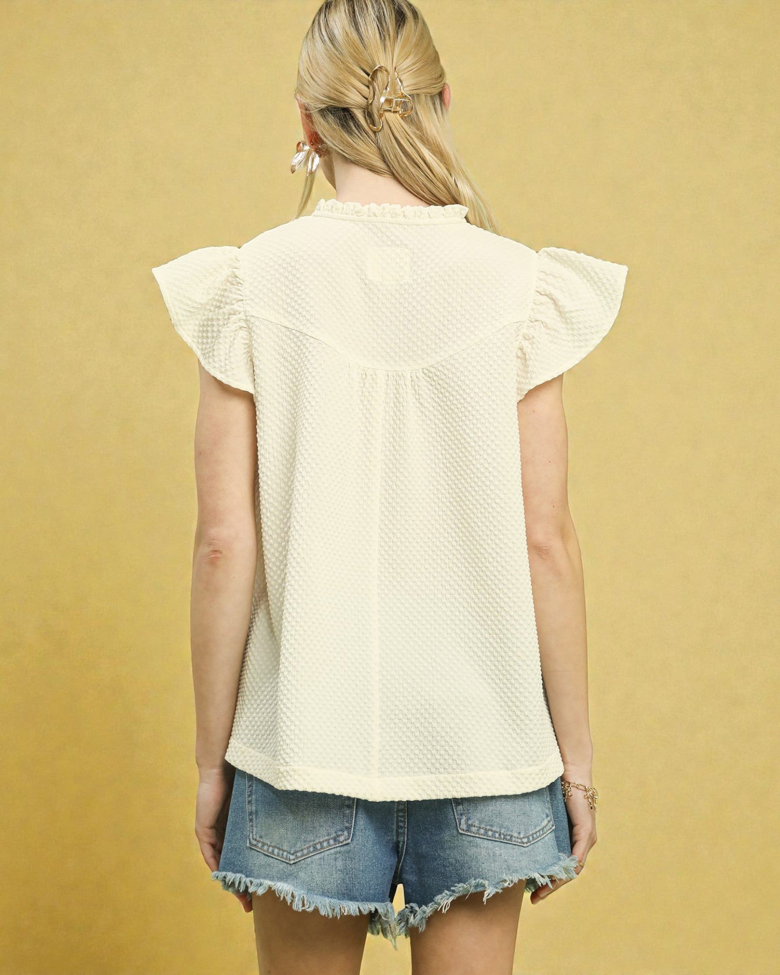 Woman wearing a light-colored top and denim shorts against a yellow background