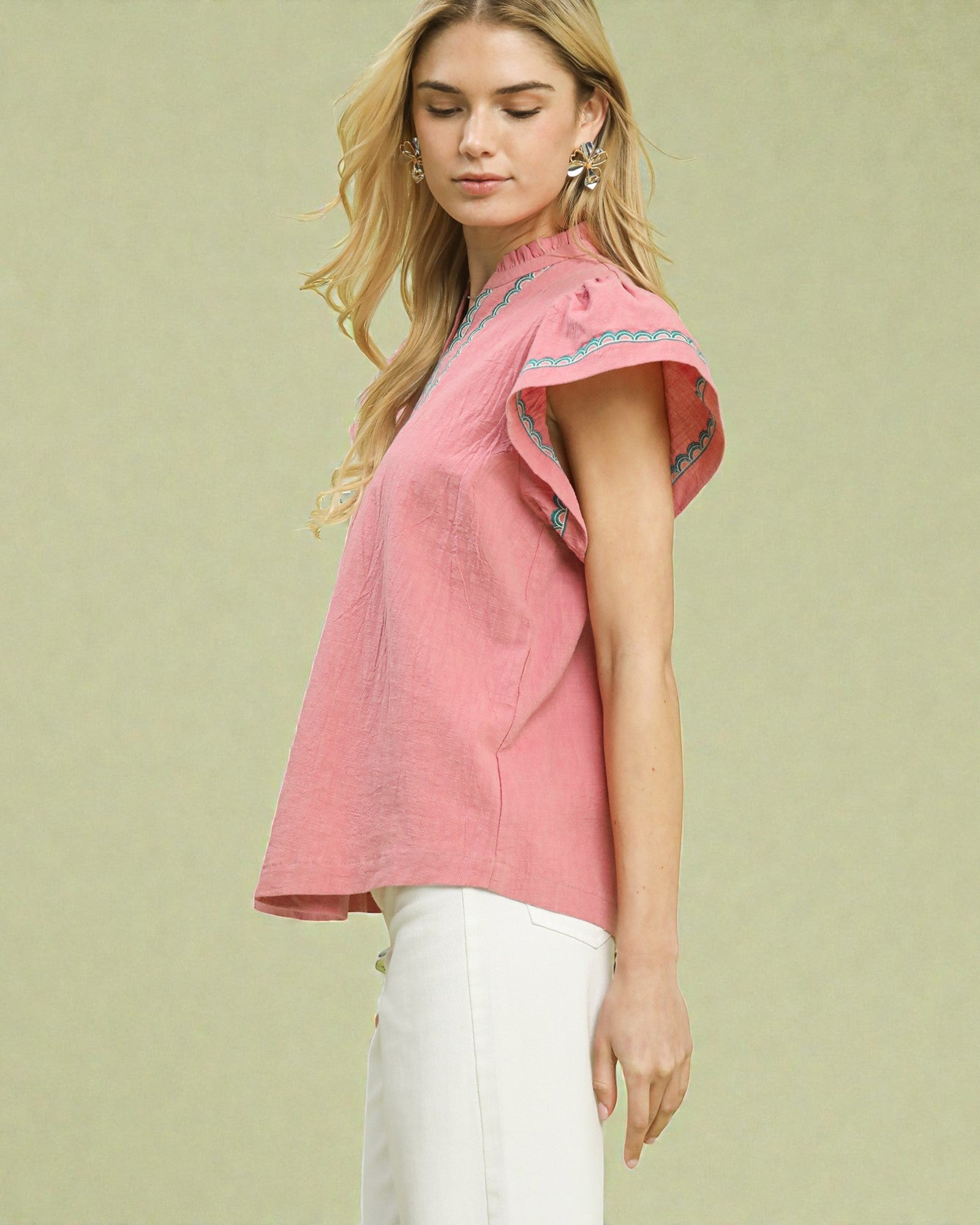 Woman wearing a pink top with embroidered details on a light green background