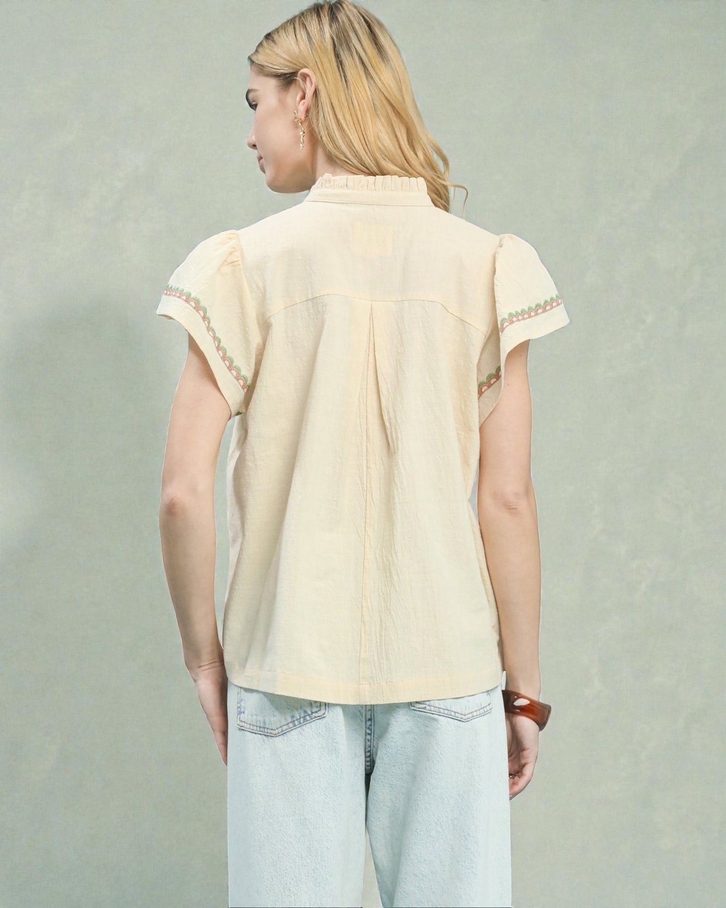 Person wearing a beige blouse with lace details on a plain background