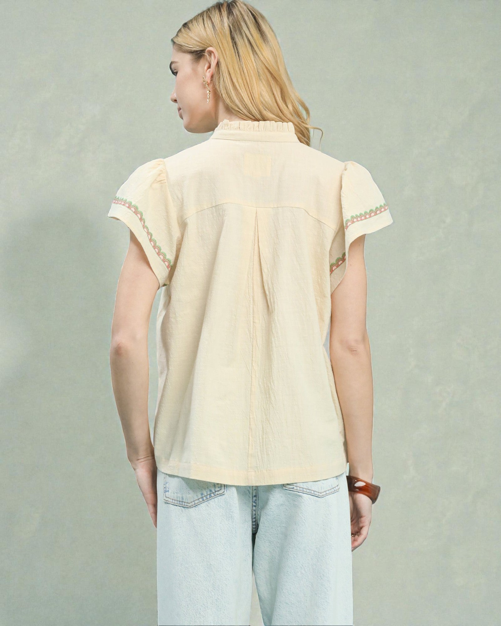 Person wearing a beige blouse with lace details on a plain background