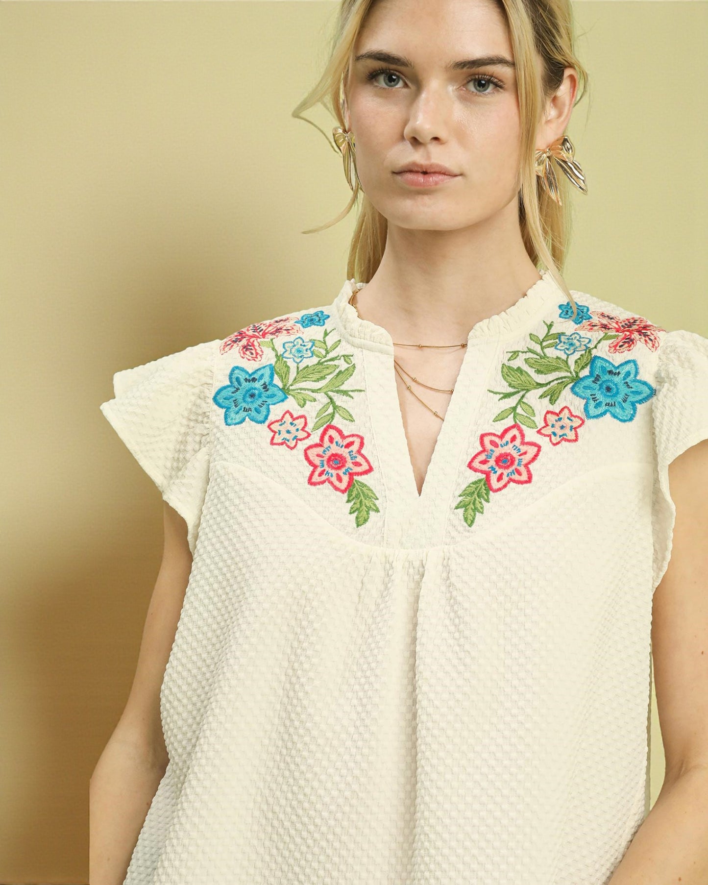Woman wearing a white top with colorful floral embroidery on a beige background