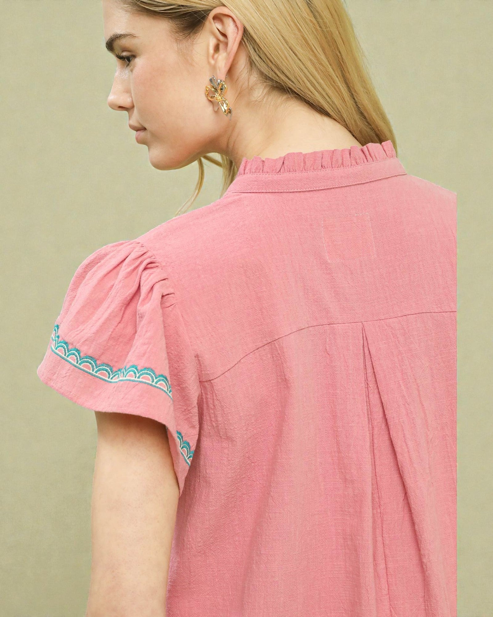 Woman wearing a pink blouse with embroidered sleeves on a beige background