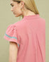 Woman wearing a pink blouse with embroidered sleeves on a beige background