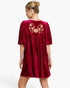 A woman shown from the back wearing a deep burgundy velvet mini dress with short puff sleeves and a floral applique detail on the upper back, set against a plain white studio background.