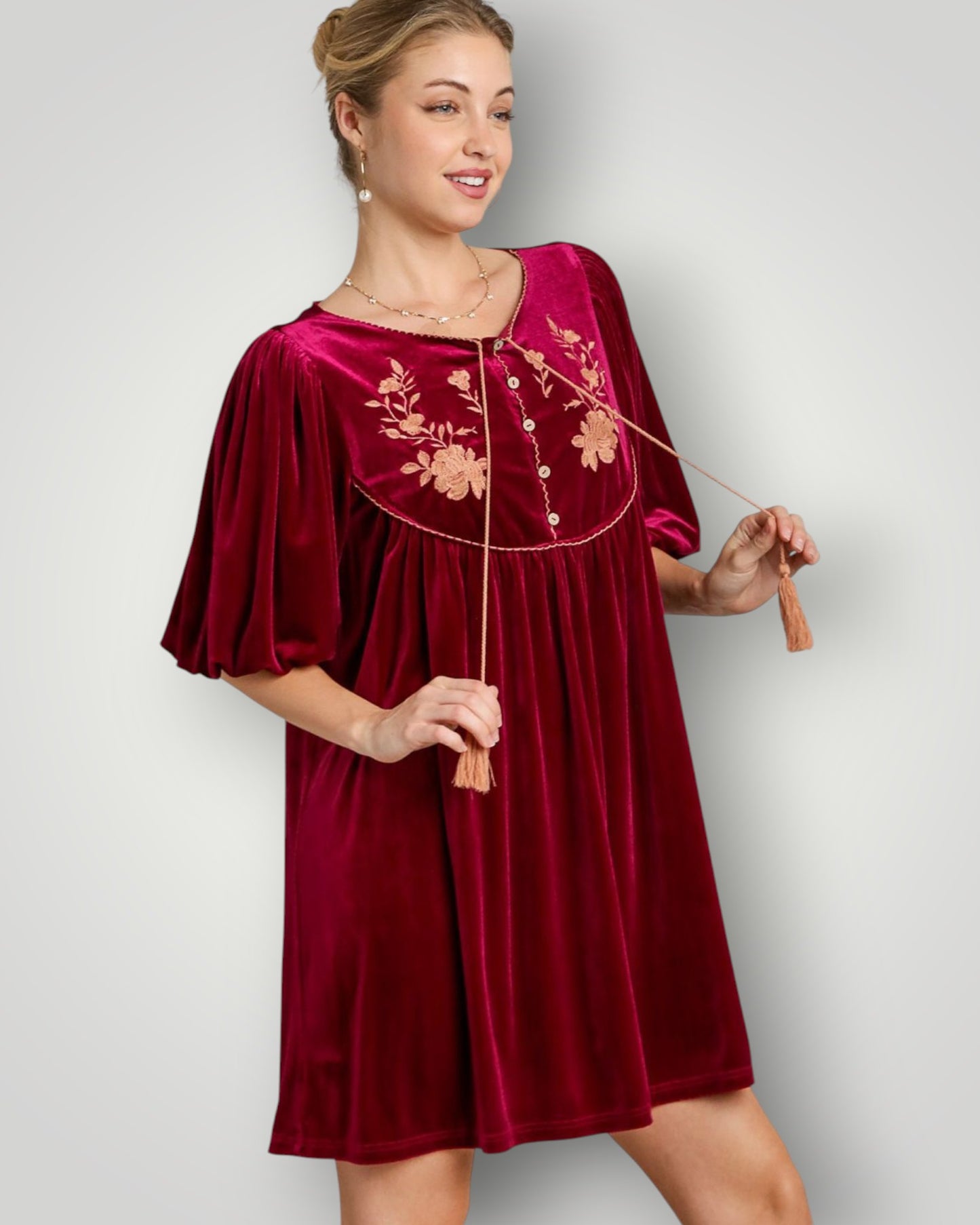Woman wearing a burgundy velvet dress with floral embroidery on a plain background