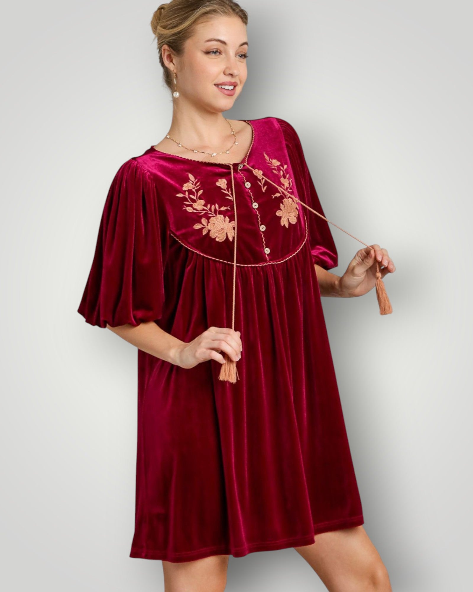 Woman wearing a burgundy velvet dress with floral embroidery on a plain background
