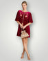 Woman wearing a burgundy dress with floral embroidery holding a beige handbag on a light gray background