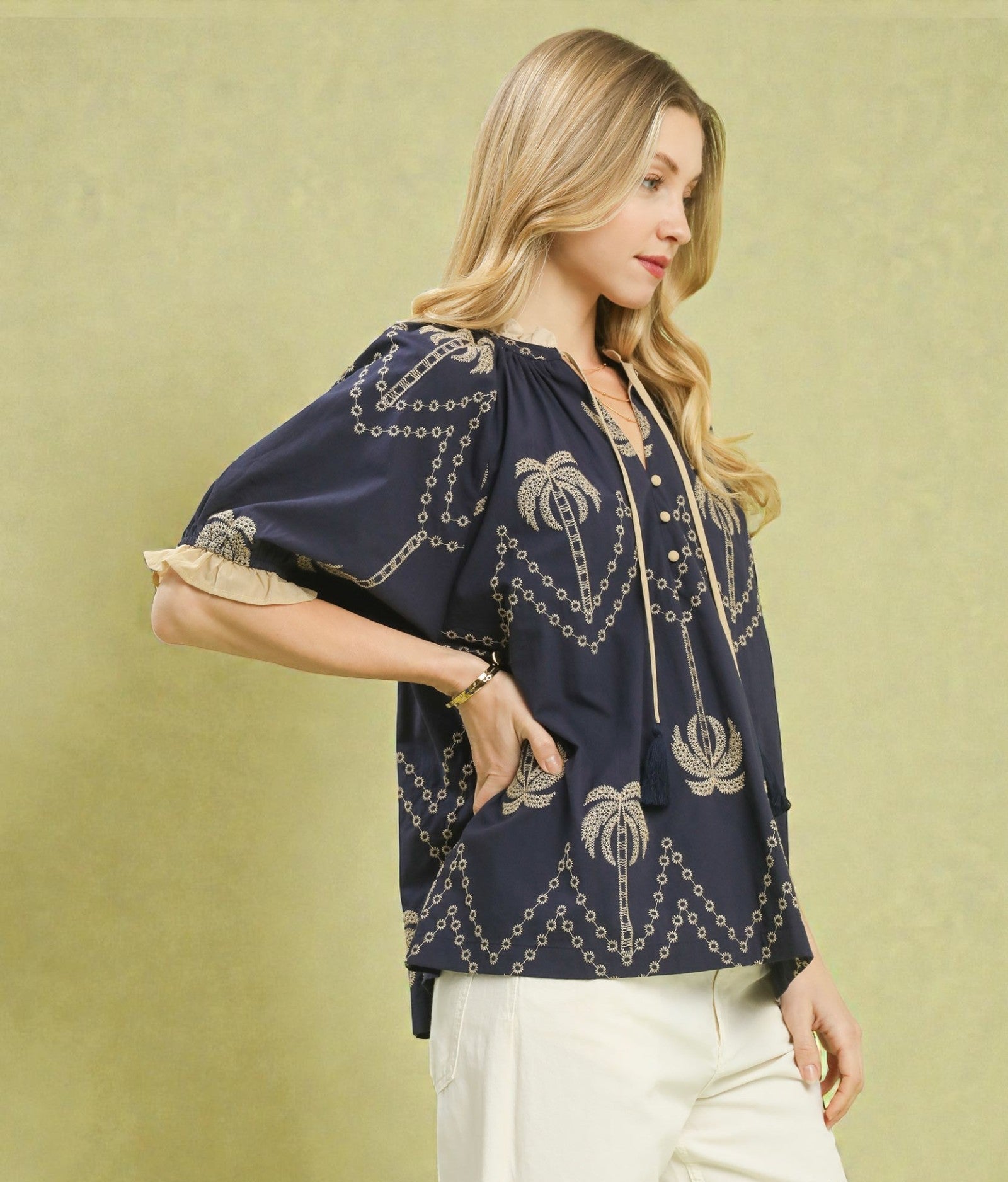 Woman wearing a navy blue embroidered blouse with white pants against a green background