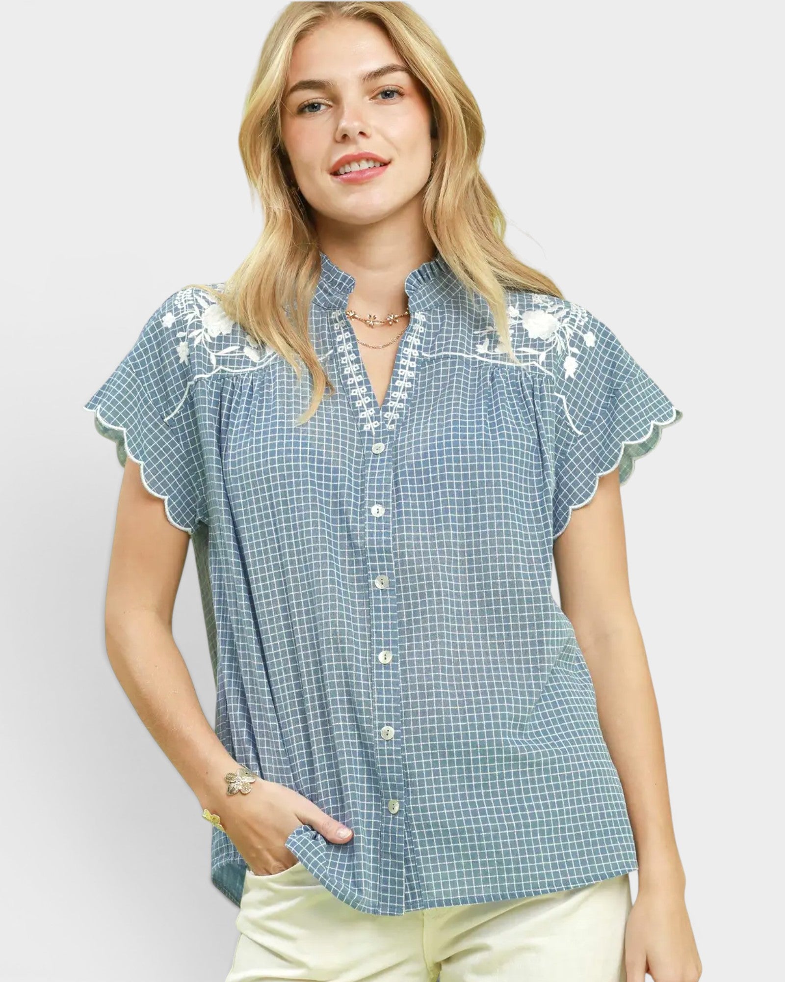 Woman wearing a blue checkered blouse with white embroidery on a light gray background