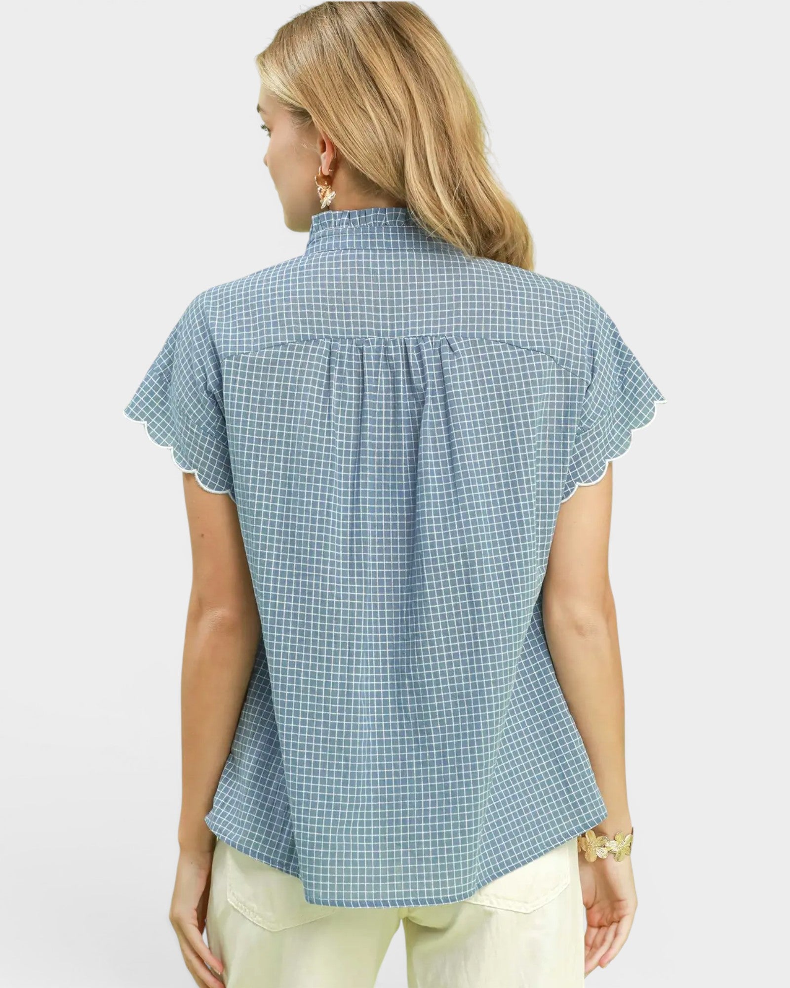 Woman wearing a blue checkered blouse with white embroidery on a light gray background