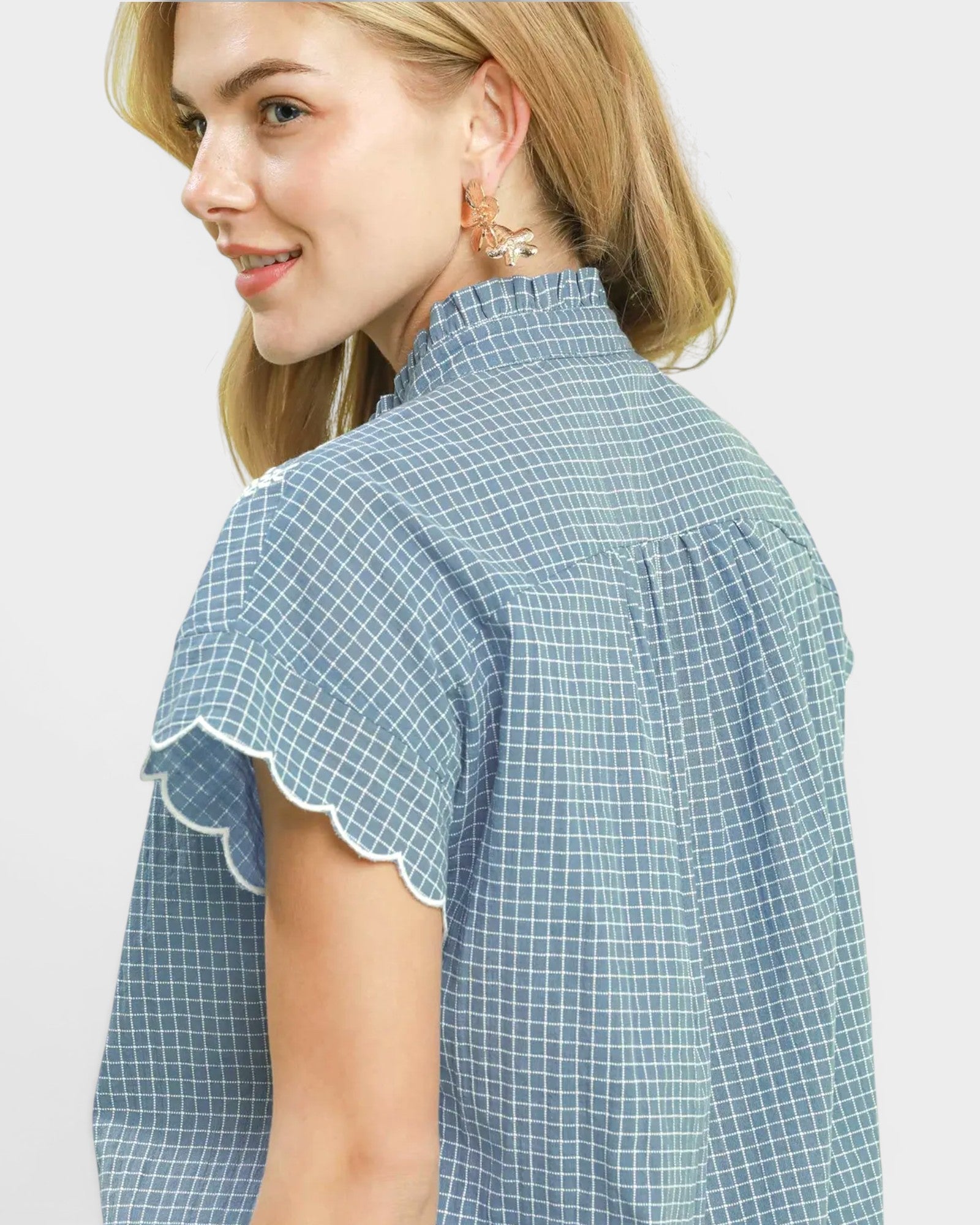 Woman wearing a blue checkered blouse with ruffled sleeves on a light gray background