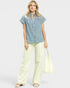 Woman wearing a blue checkered shirt with lace details and light yellow pants on a white background