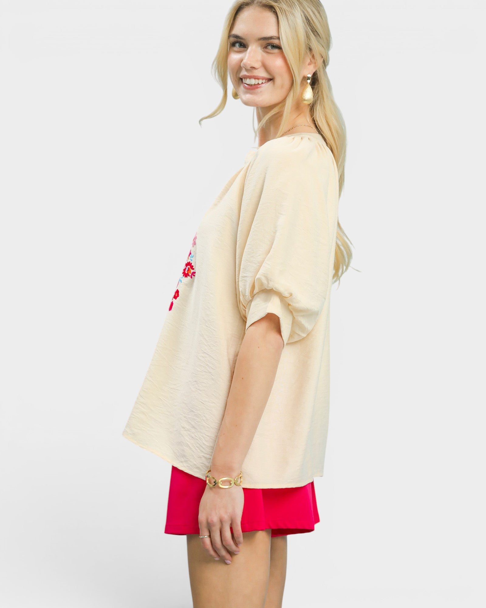 Woman wearing a beige cardigan with floral design and red shorts on a white background