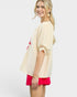 Woman wearing a beige cardigan with floral design and red shorts on a white background