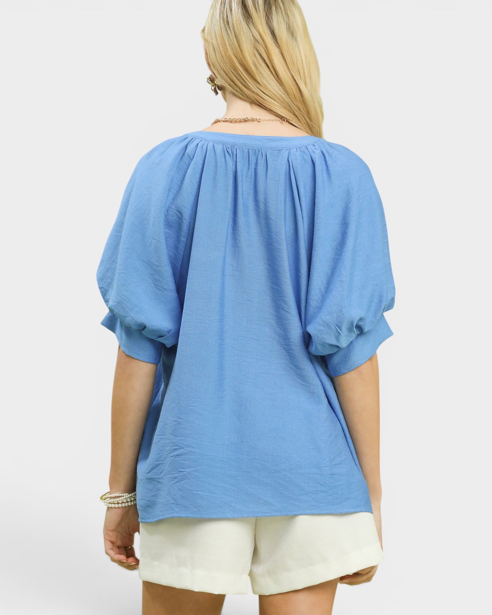 Woman wearing a blue blouse and white shorts on a light gray background