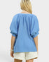 Woman wearing a blue blouse and white shorts on a light gray background
