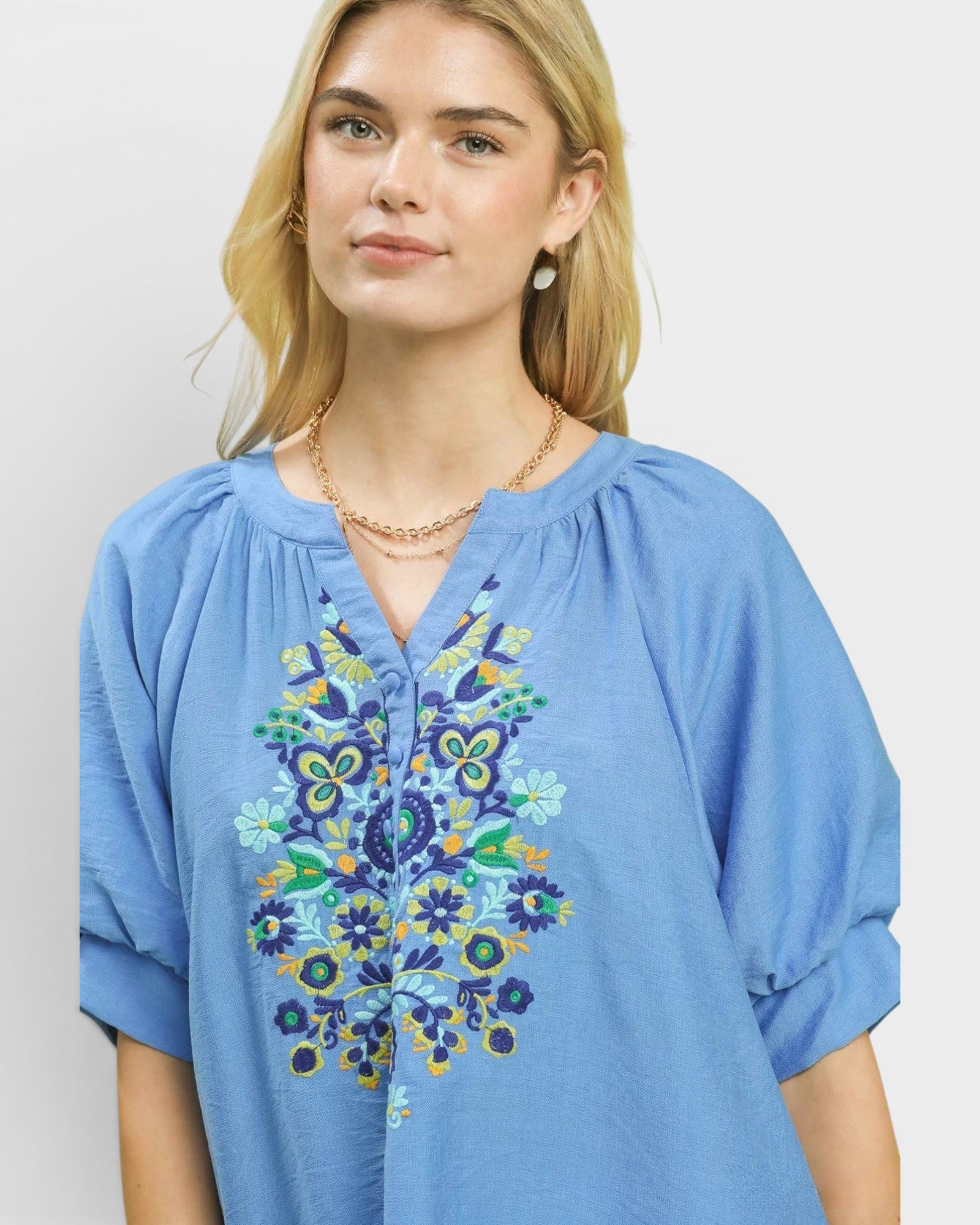 Woman wearing a blue embroidered blouse against a plain background