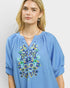 Woman wearing a blue embroidered blouse against a plain background