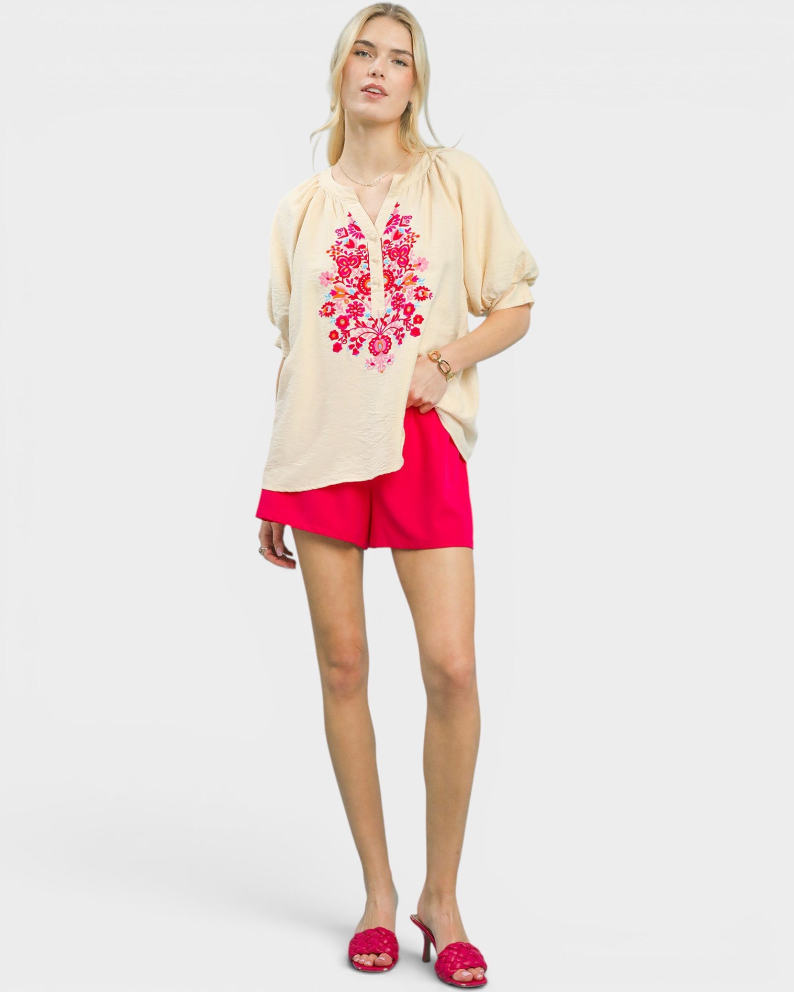Woman wearing a beige blouse with floral embroidery and pink shorts on a white background