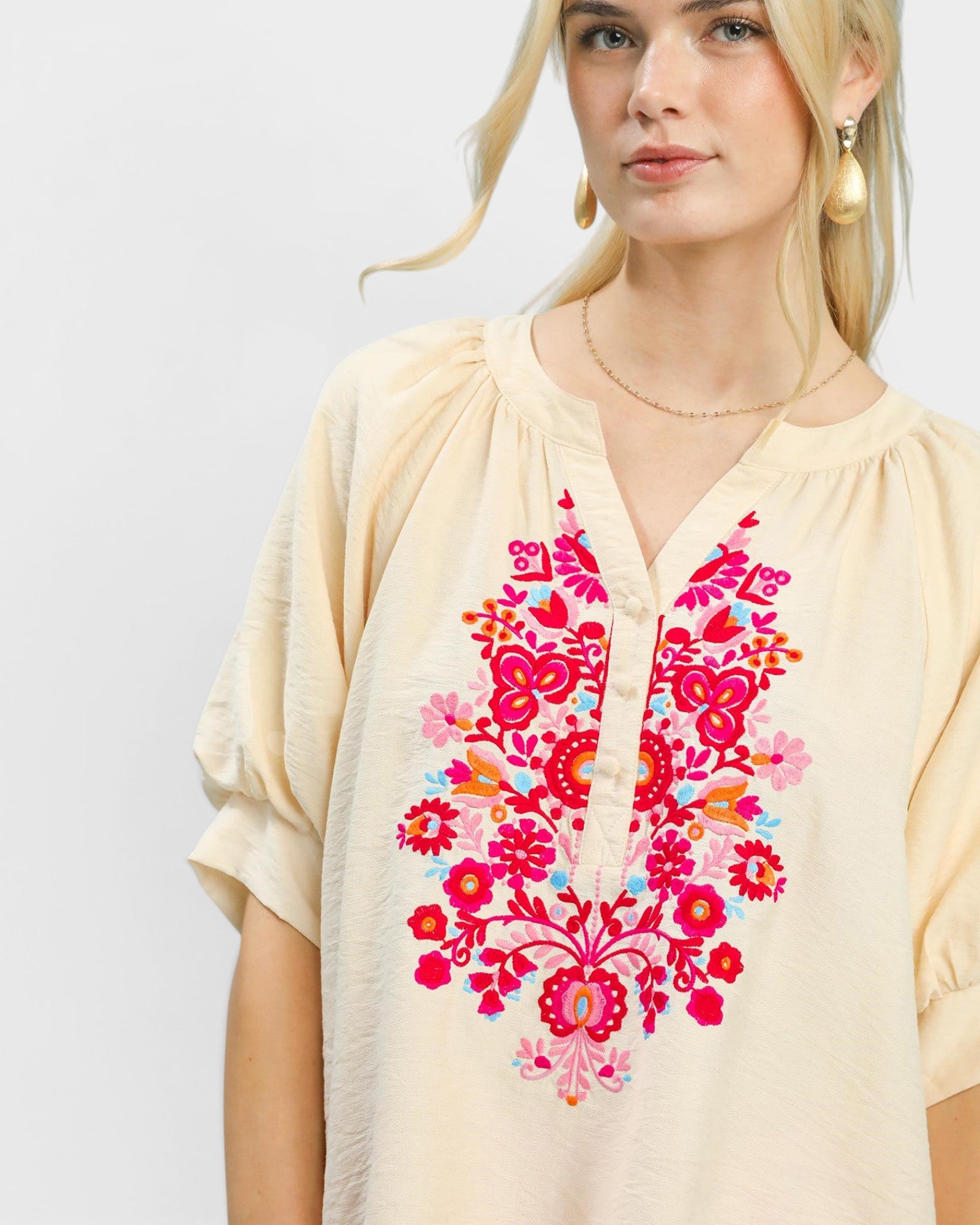 Woman wearing a beige blouse with colorful floral embroidery on a plain background