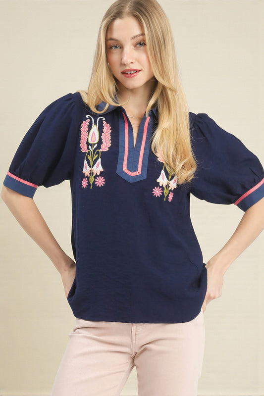 Woman wearing a navy blue blouse with floral embroidery on a beige background