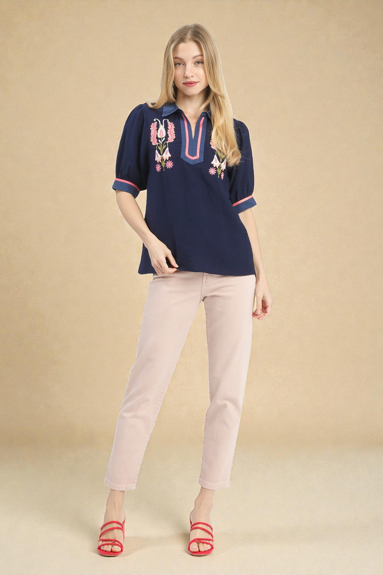 Woman wearing a navy embroidered blouse and light pink pants on a beige background