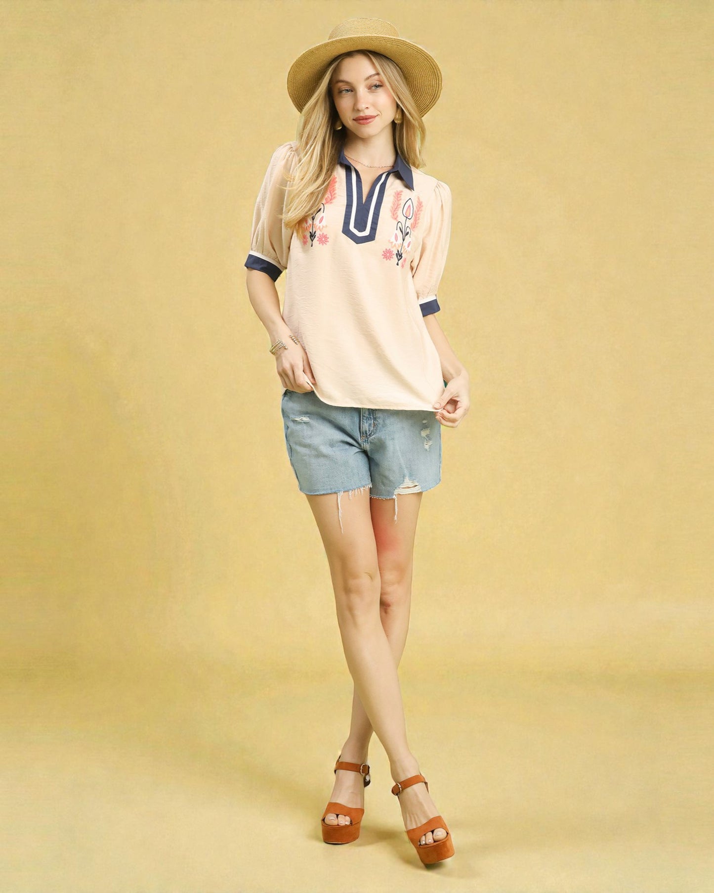 Woman wearing a beige polo shirt with colorful designs and denim shorts on a yellow background