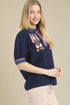 Woman wearing a navy blue blouse with floral embroidery on a beige background